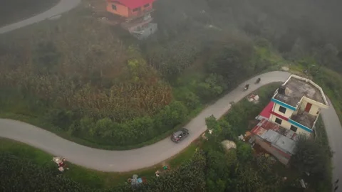 Drone shot of vehicles moving on the road, middle of a rural, green village Stock Footage 287933900