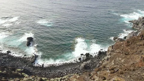 Drone shot of a volcanic cliff with ocean waves breaking on a rocky shore Stock Footage 193674151