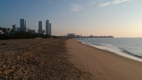Drone shot of waves along the beach line at sunrise, with city skyline in the BG Stock Footage 94482079