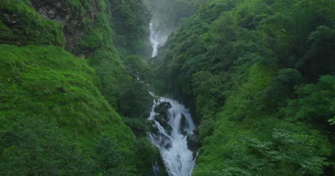 Drone shot of white mountain waterfall cascading down lush green gorge in Stock Footage 345275383