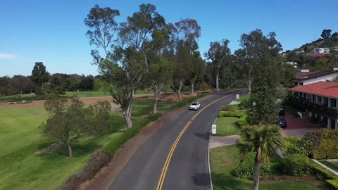 Drone Shot of White SUV Driving on Scenic Suburb Road Next to Golf Course Vídeo Stock 340565692