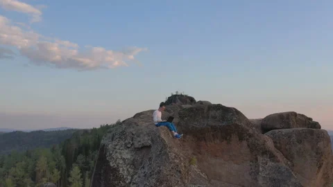 Drone shot of a young man working on a laptop sitting on the edge of a rock Video stock 131083735