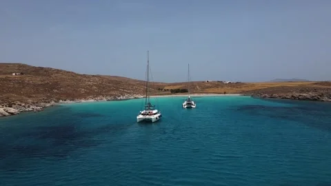 Drone side flyby of catamarans anchored in turquoise Greek bay Stock Footage 308106887