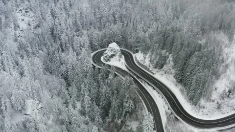 Drone side pan over winding mountain road with cars in snowy forest landscape Video stock 331986885