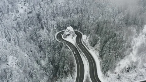 Drone side pan over winding mountain road with cars in snowy forest landscape Video stock 331987470
