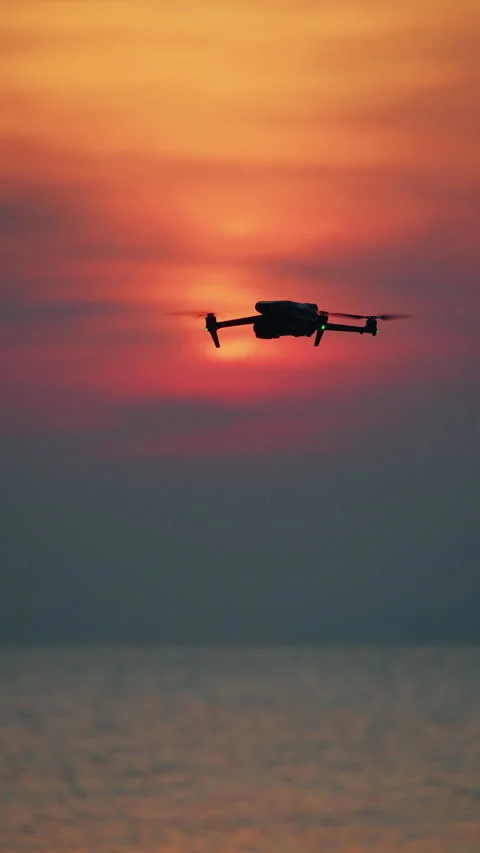 Drone silhouette hovering over sea at sunset with soft red orange sky Stock Footage 332107861
