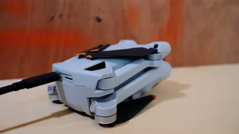Drone sitting on desk charging via USB-C cable, battery indicator flashing green Видео 219774642