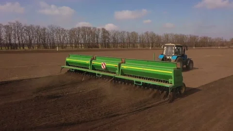 Drone sliding shot of a farmer in tractor seeding, sowing agricultural crops at Stock Footage 236951540