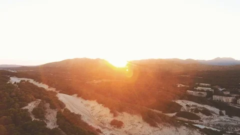 Drone slow reveal of red sunset with sun flare over forest and beach landscap Stock Footage 101566419