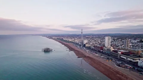 Drone slowly flies back from empty beach, calm sea and Brighton at dawn Stock Footage 192400742