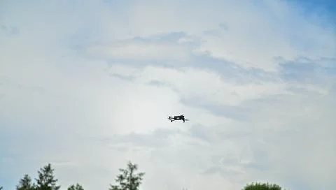 Drone is soaring through a clear sky, with a backdrop of white clouds and d.. Stock Photos