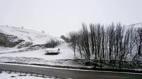 The drone soars above undulating terrain and icy roads amidst a gentle snowfall Stock Footage 263358260