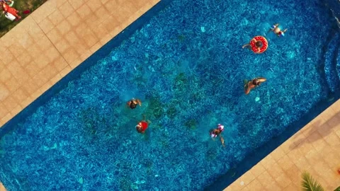 Drone spirals upward capturing resort pool scene with people swimming and 動画素材 308577752