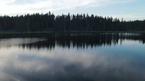 Drone starting low the rising while flying over a calm small lake surrounded by Stock Footage 328171748