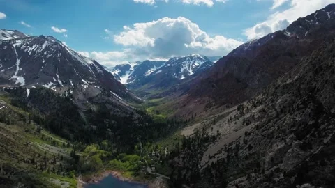 Drone takes off over gray mountains with white peaks, valley and Lundy Lake Video stock 136060965
