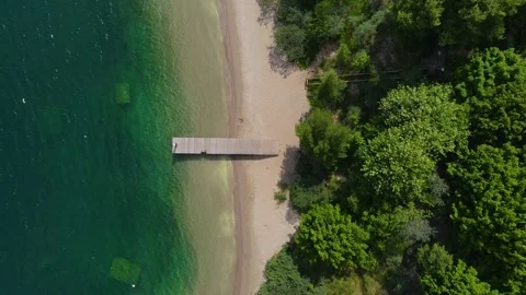 Drone takes off over pier with walking man on the turuoise water lake Stock Footage 155930862