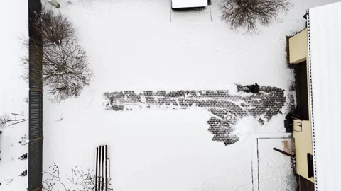 Drone top-down of a homeowner pushing slush off a cobblestone strip beside a Stock Footage 328357925