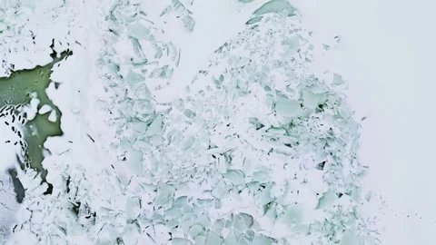 Drone top-down view of jagged sea ice ridges and broken slabs near a rocky Stock Footage 331011342