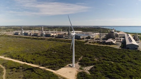 Drone tracking back to reveal wind turbine with aluminum smelter in background. Stock Footage 88305024