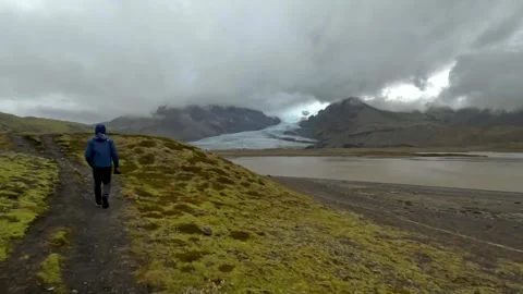 Drone tracking a man walking along a trail with a glacier in the background Stock Footage 345126858