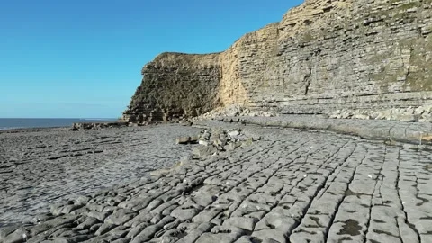 Drone tracking shot across rocks at the bottom of a cliff by the sea Stock Footage 248068033