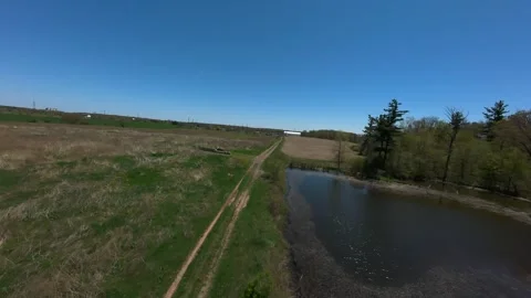 Drone tracking shot flying over a dirt road next to a country pond 스톡 동영상 341815448