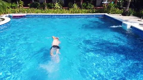 Drone tracking shot over a man swimming in a blue pool in a resort on summer day Stock Footage 148973362