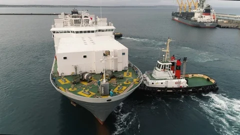 Drone tracking in on tugboat pushing ship into position on busy wharf. Stock Footage 87852519