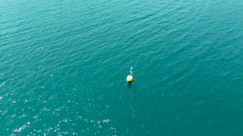 Drone Tracking Yellow Buoy in Clear Blue Water with Mountain Views – 4K Aerial Stock Footage 313900674