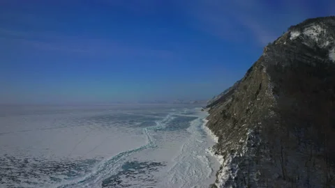 Drone turn around over gray rock with winter trees, reveal endless ice coastline Stock Footage 166433377