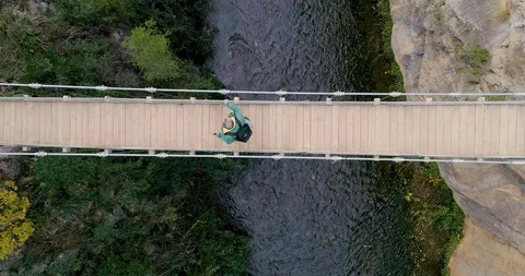 Drone upward flight and overhead view of suspension bridge and senior hiker Stock Footage 124386961