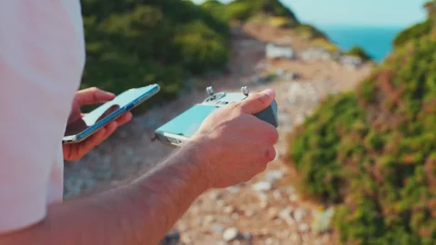 Drone use on a coastal path during a sunny day by a person holding a remote Stock Footage 338244181