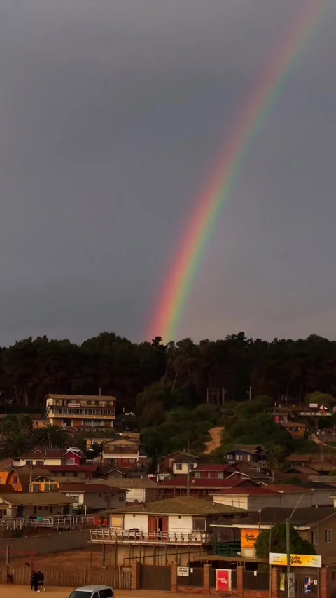 Drone Vertical Panning Shot of a Rainbow Over Coastal Village Houses at Sun.. Vídeos de archivo 339252225