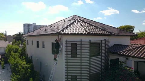 Drone video of a builder stands on a high ladder next to a nice house 4k Stock Footage 234910282