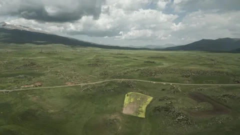 Drone video. Fields between green stony hills. Snowy mountain tops. Stock Footage 252018000
