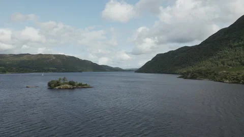 A drone video over a lake surrounded by mountains with a tiny island. Stock Footage 251597388