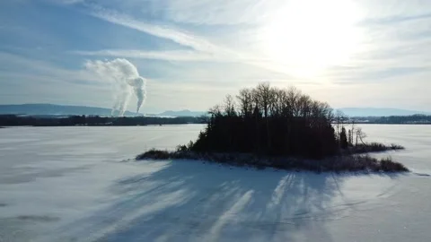 Drone video rotating around a island on a frozen lake with factory smoke. Stock Footage 303678258