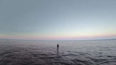 Drone video of a single man standing in the middle of the sea looking at the Stock Footage 249626621