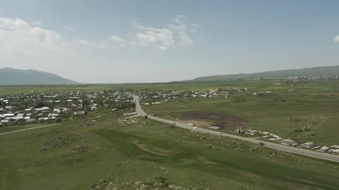 Drone video. Village between green stony hills, snowy mountain tops, road. Video stock 252020853
