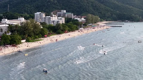 Drone view of Batu Ferringhi Beach shows more visitors enjoying water sports Видео 332151436