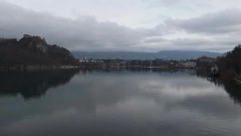 Drone view of Bled Castle above winter lake with mountains under overcast skies Stock Footage 336467652