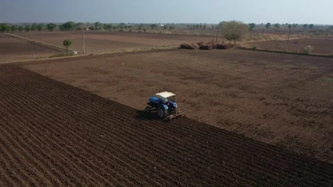 Drone view capturing a blue tractor tilling a vast agricultural field, creating Stock Footage 337198980