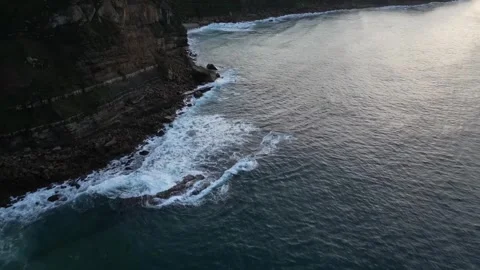 Drone view of coastal cliffs and ocean waves approaching shoreline at sunset Stock Footage 317447830