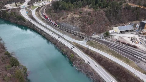 Drone view of colorful train arriving at station over river with traffic 스톡 동영상 330749054