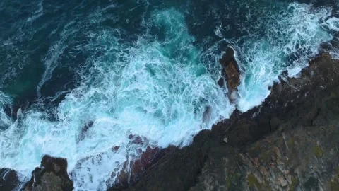 Drone view of crashing ocean waves hitting rocky coastline with swirling foam an Stock Footage 308934345