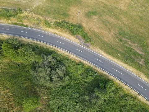 Drone view of a curved road between grass and trees in the landscape Stock Photos