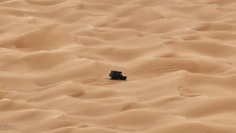 Drone view of a dark Range Rover Classic driving across the vast sand dunes of 動画素材 335165846