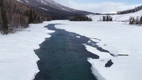 Drone view following blue river through frozen snowy landscape in Xinjiang Stock Footage 336604455