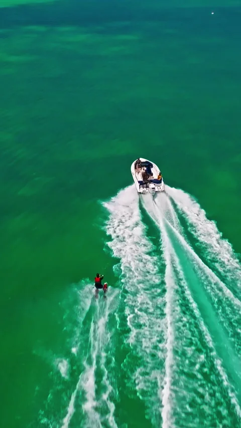 A drone view of a guy skiing behind a speedboat on crystal-clear water. Extreme Stock Footage 342961083