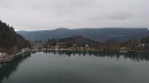 Drone view of Lake Bled's winter water with hills and mountains under grey sky Stock Footage 336467692